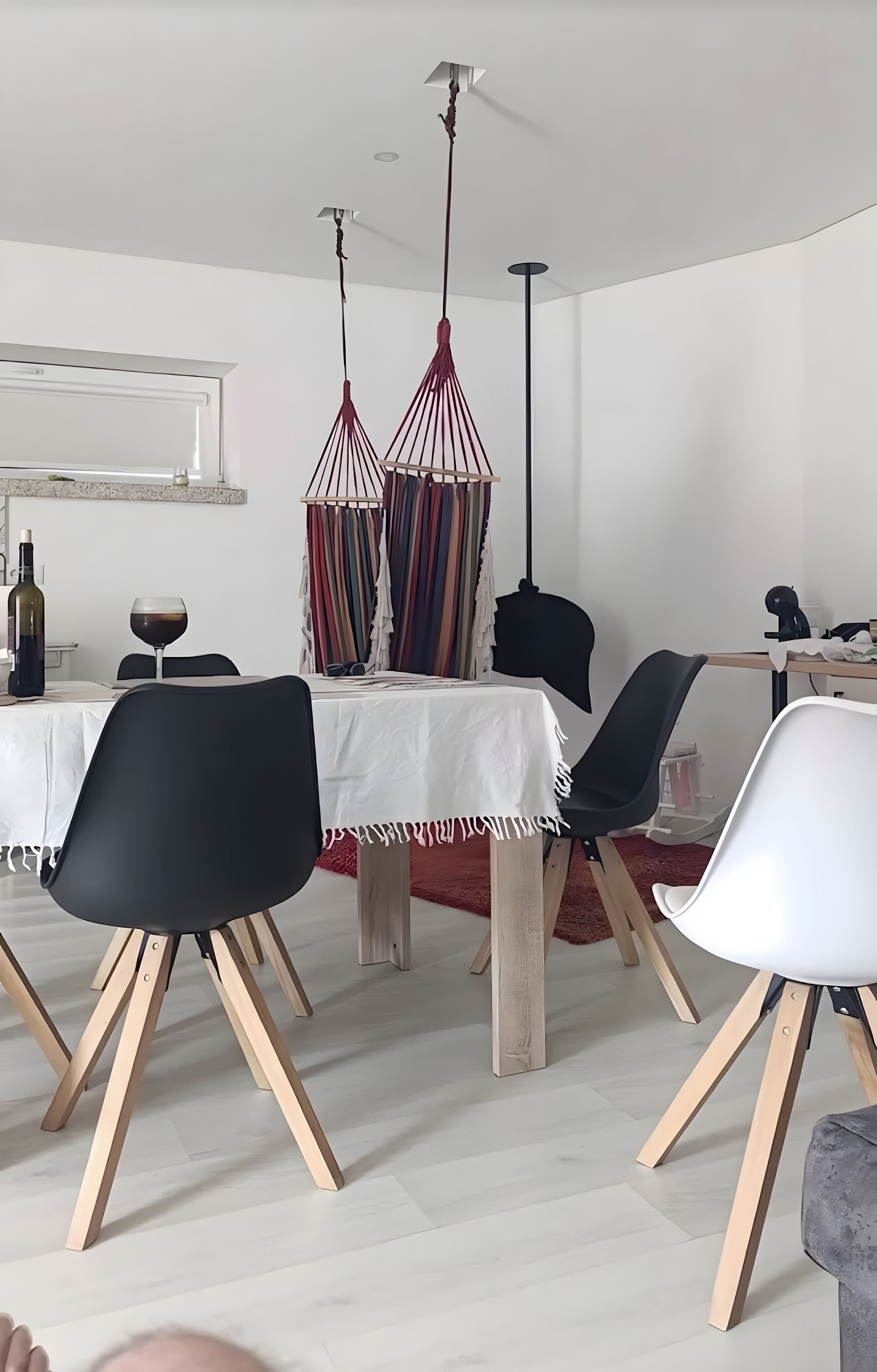 Comedor con mesa blanca, sillas negras y lámpara colgante.