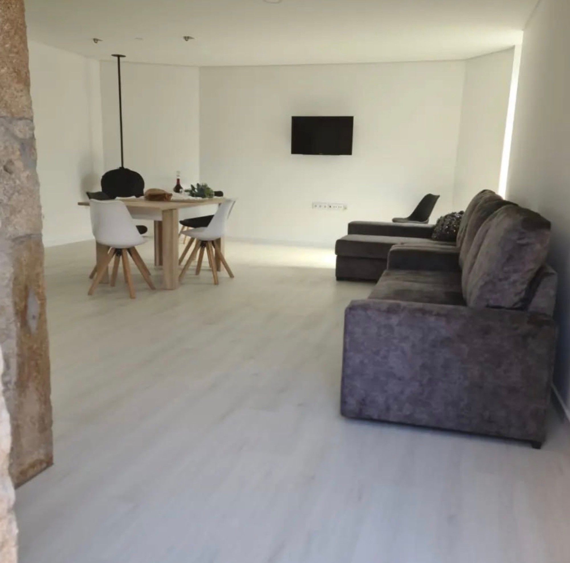 Un salon moderne avec un canapé gris, un coin repas comprenant une table et des chaises, et un téléviseur à écran plat fixé au mur.