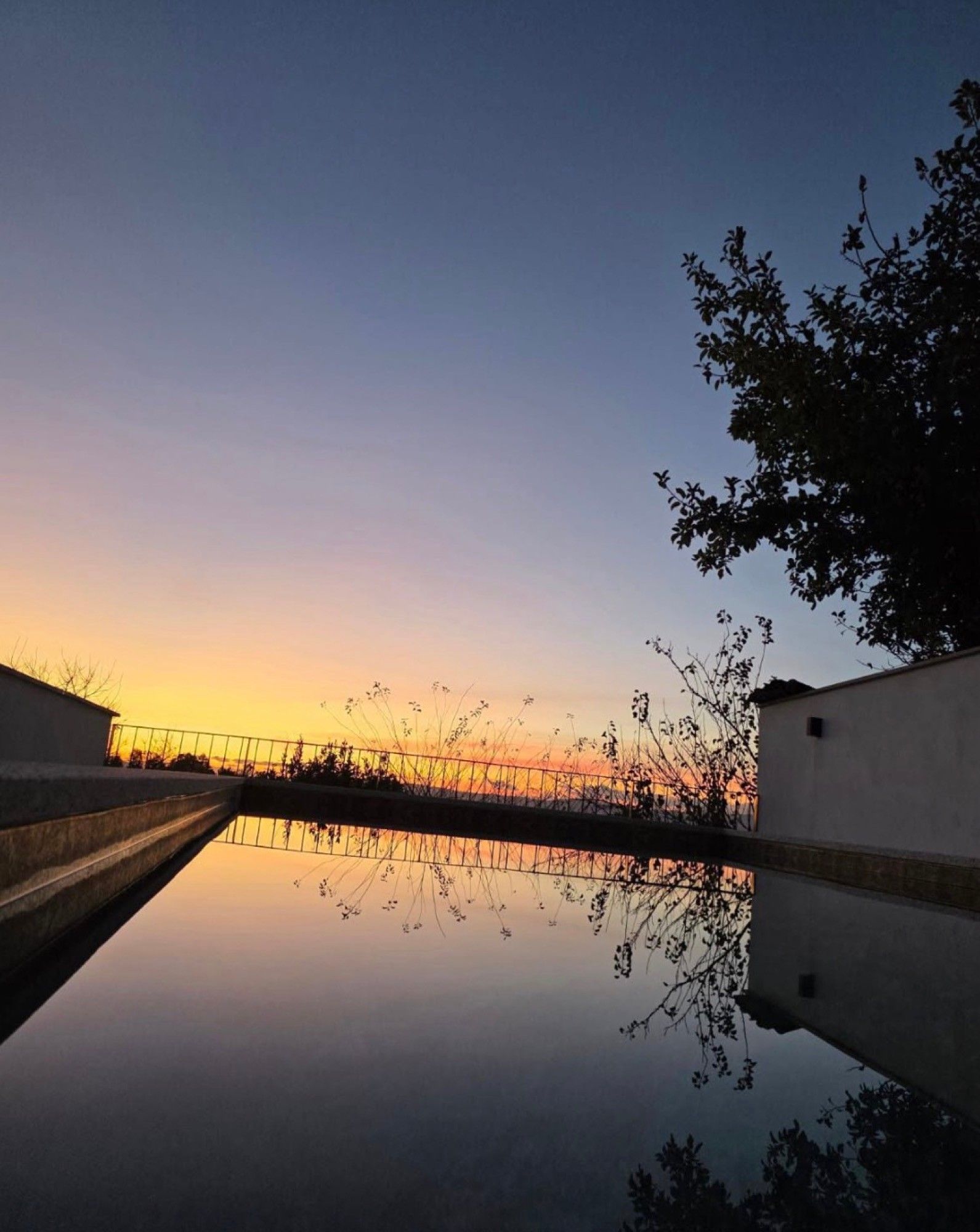 Una masa de agua tranquila reflejando un atardecer, con un puente y edificios al fondo.