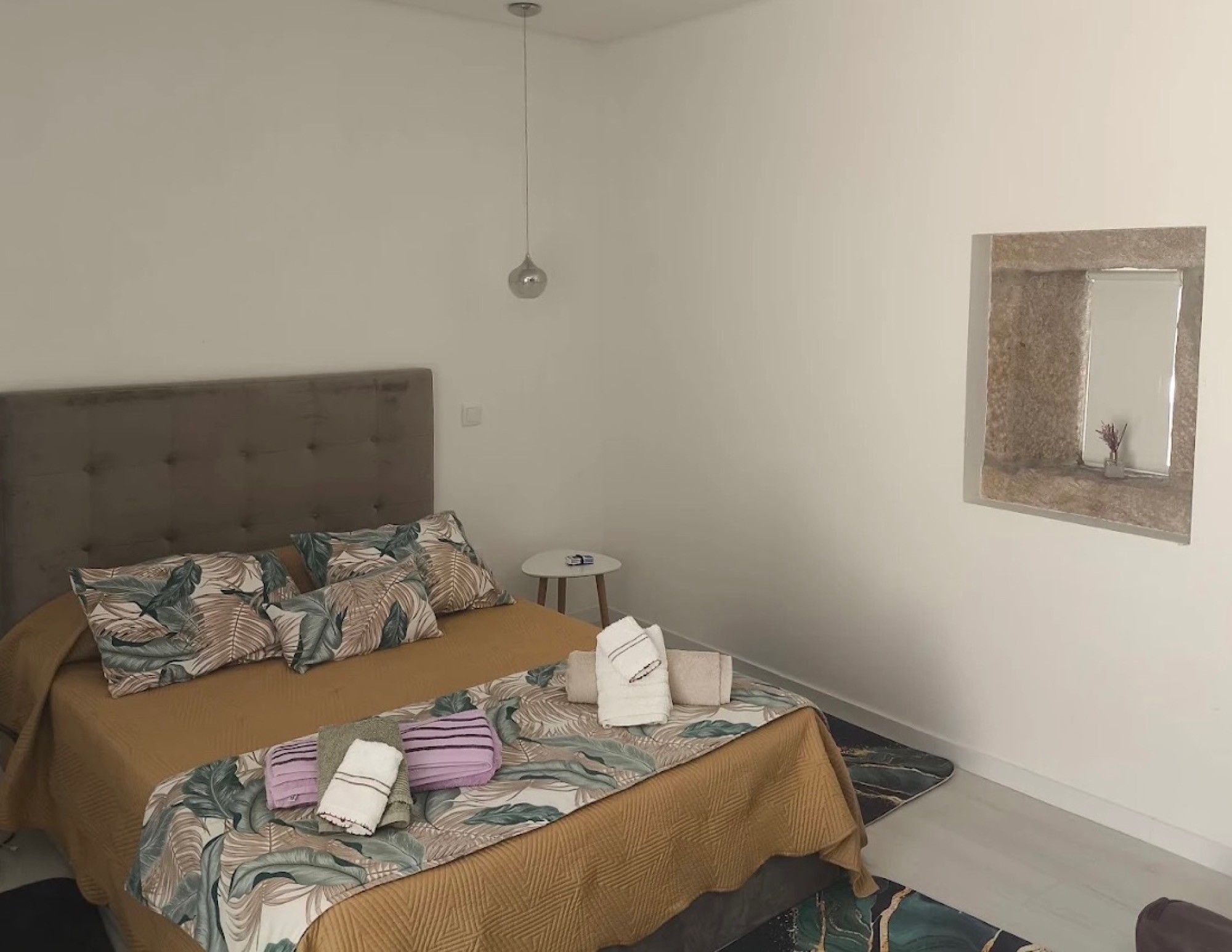 Une chambre à coucher avec un lit, une table de chevet, une lampe suspendue et un miroir au mur.