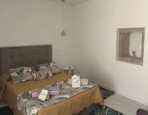 Une chambre à coucher avec un lit, une table de chevet, une lampe suspendue et un miroir au mur.