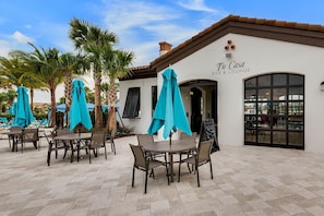 An outdoor seating area with tables and chairs, covered by umbrellas, and a building labeled 'Tu Casa Bar & Lounge' with a pool visible in the background. - 5BR Townhome Near Disney Pool, by Clubhouse (Kissimmee)