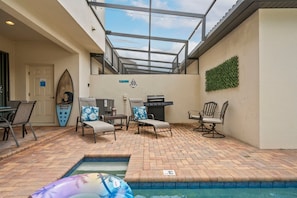 An outdoor pool area with lounge chairs, a grill, and a surfboard decoration. - 5BR Townhome Near Disney Pool, by Clubhouse (Kissimmee)