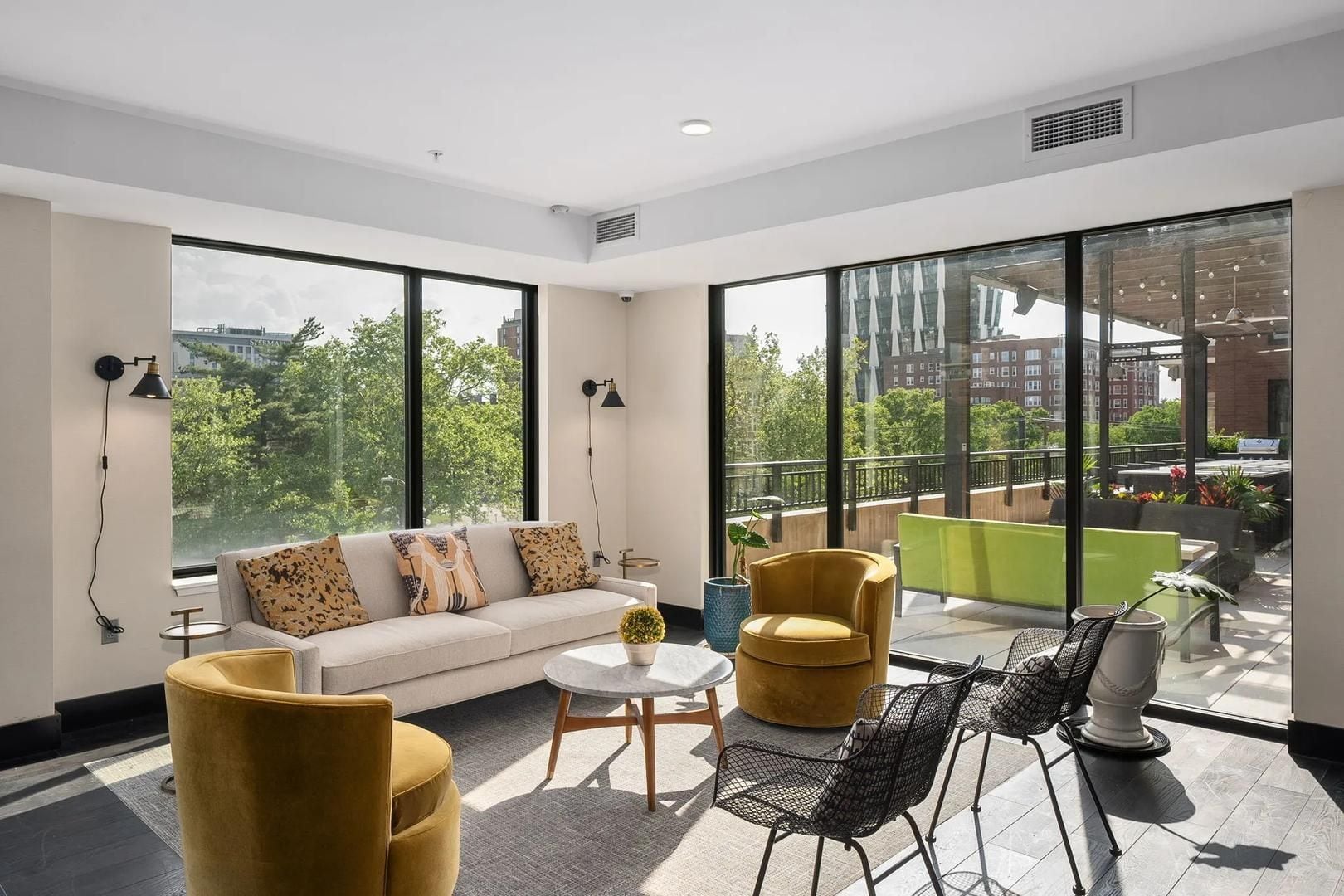 A modern living room with a sofa, armchairs, a coffee table, and a dining area with chairs. Large windows provide a view of the cityscape.
