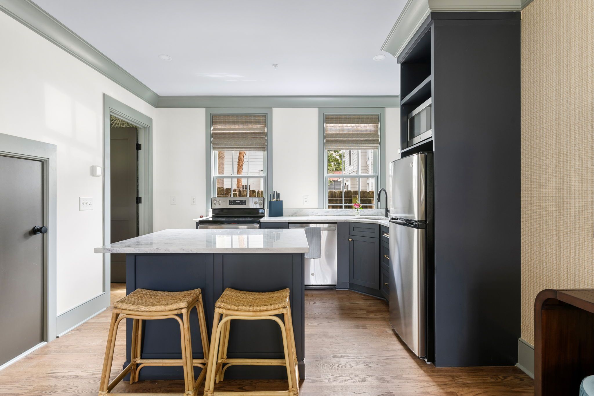 A modern kitchen with a large island, dark cabinetry, and a view through the windows.