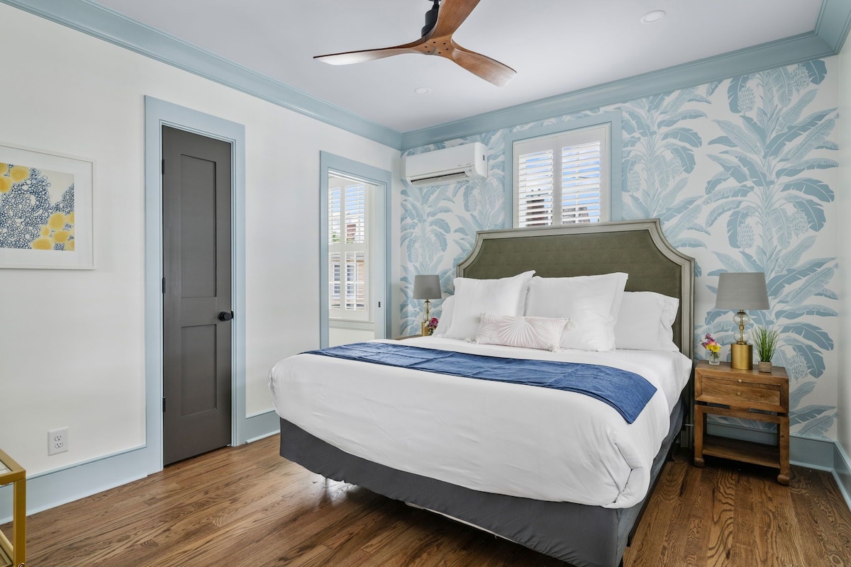 Quarto com cama, ventilador de teto, mesa de cabeceira e janela com persianas.