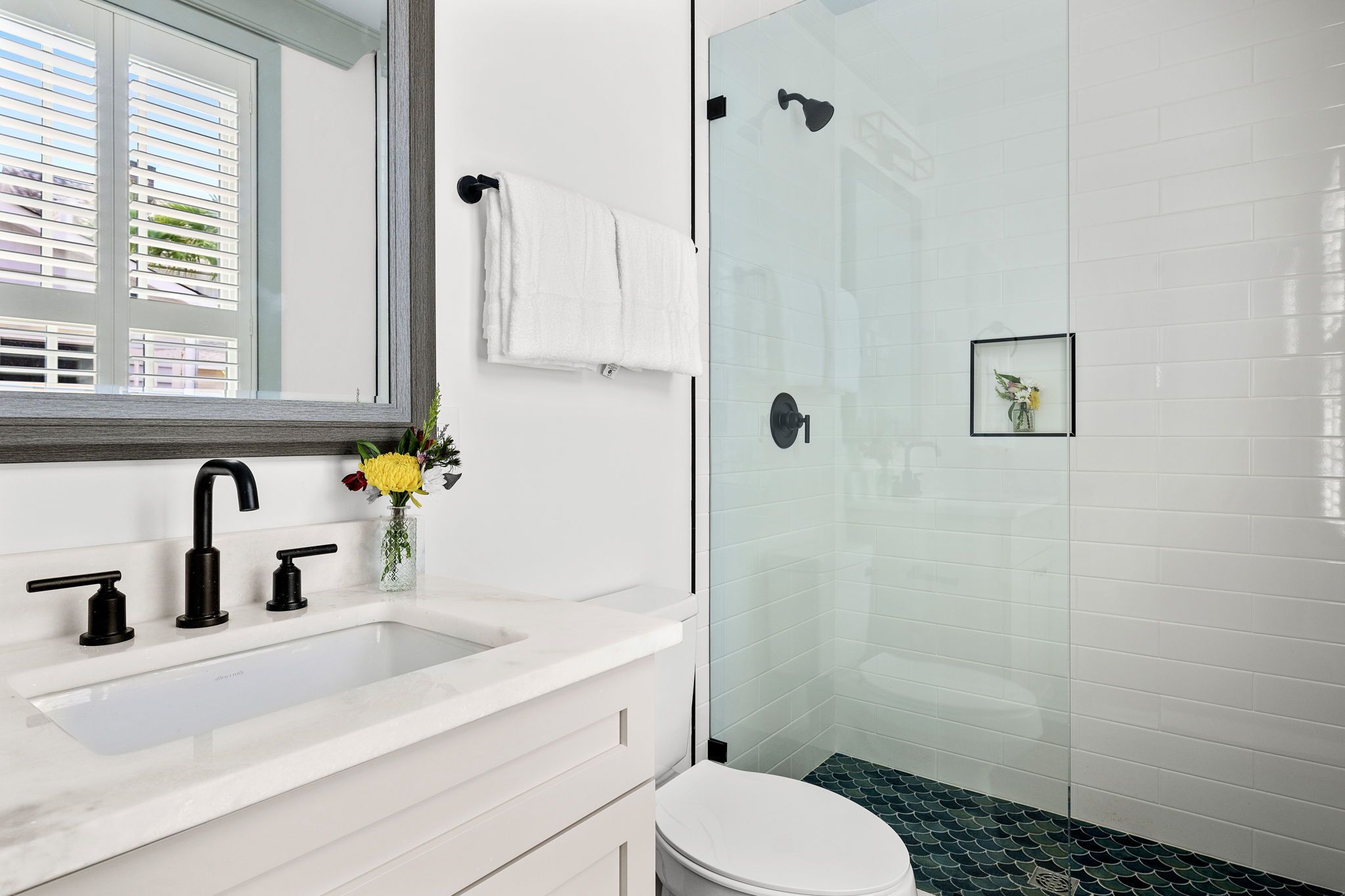 A modern bathroom with a white sink, black faucet, and a glass shower enclosure.