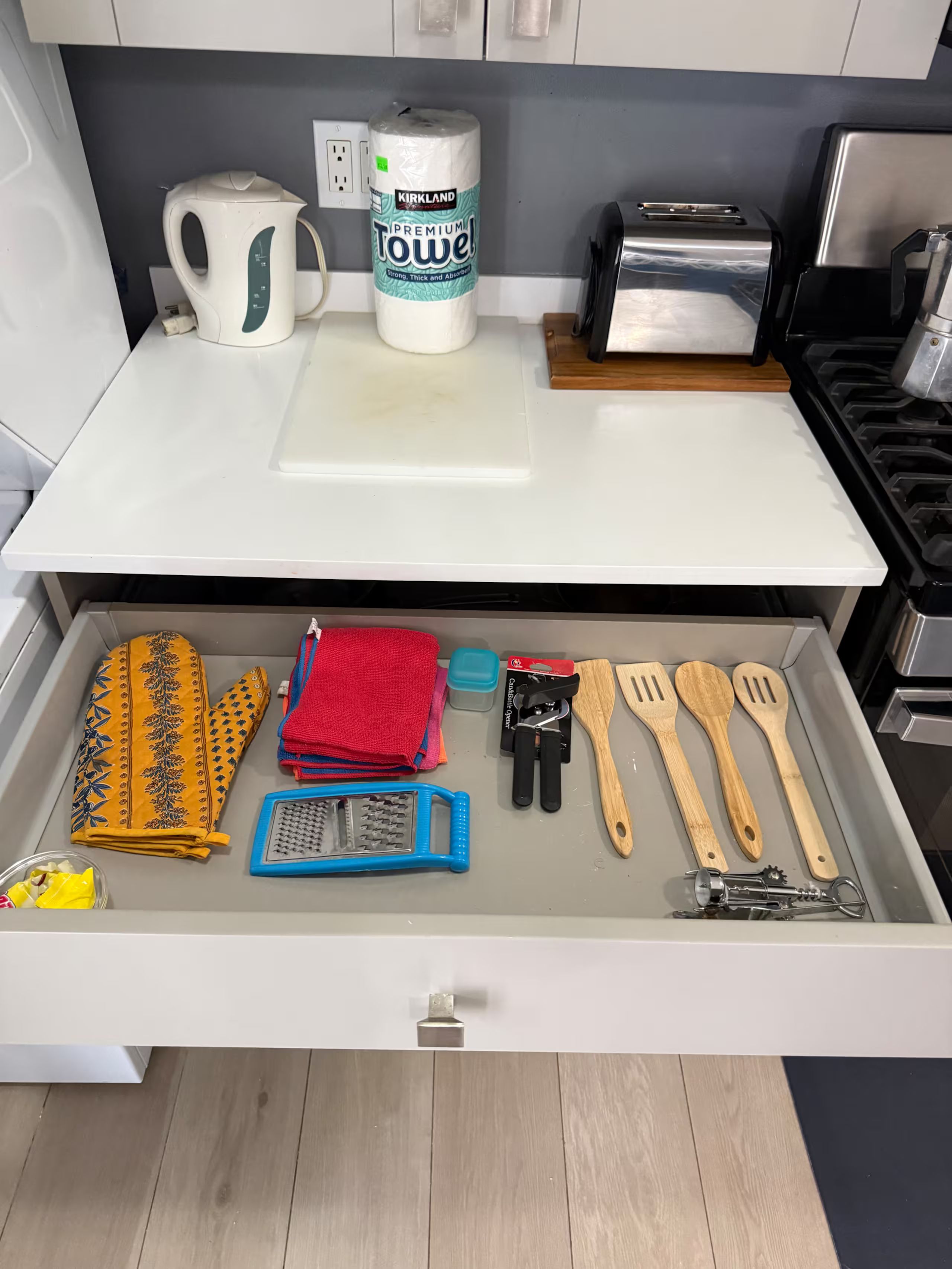 Een keuken met een wit aanrecht, een waterkoker, een rol keukenpapier en een lade met keukengerei.