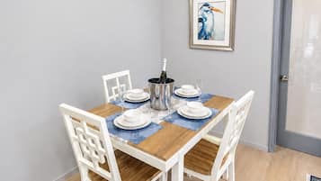A dining area with a table set for four, white chairs, a chandelier, and a framed picture on the wall.