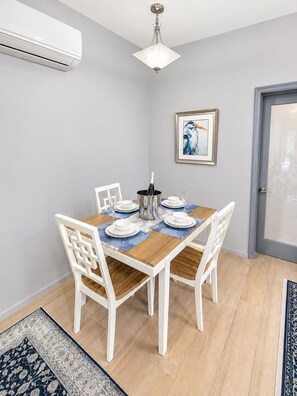 Un coin repas avec une table dressée pour quatre personnes, des chaises blanches, un lustre et un tableau encadré au mur.