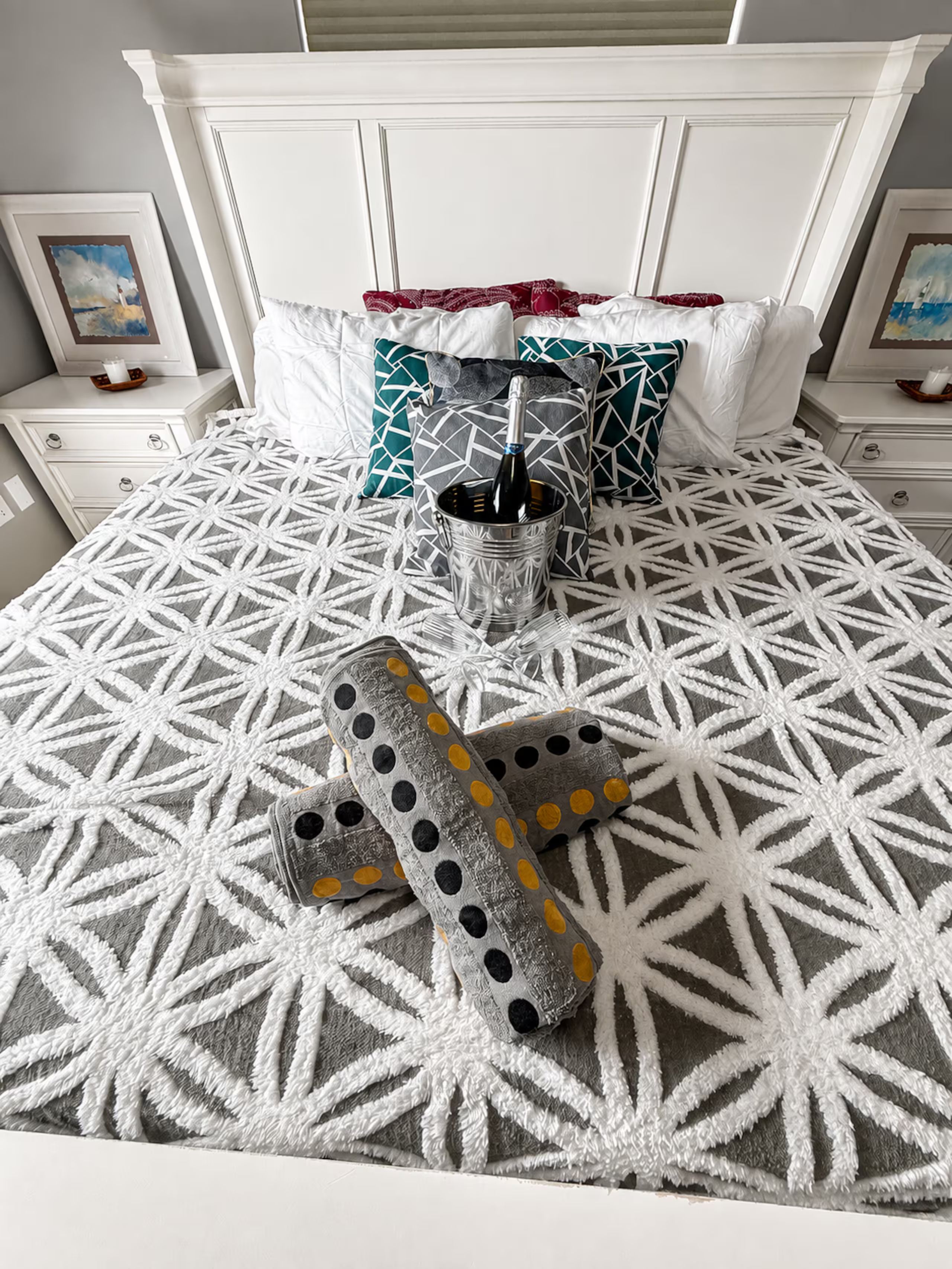 Een bed met een deken met een geometrisch patroon, een metalen emmer met een fles, en een paar slippers met een stippenmotief.