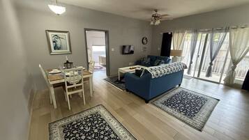 Een woonkamer met een blauwe bank, een eettafel met stoelen en een kroonluchter.