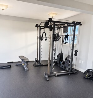 Une salle de sport équipée d’un support à squats, d’un banc et de divers disques de poids.