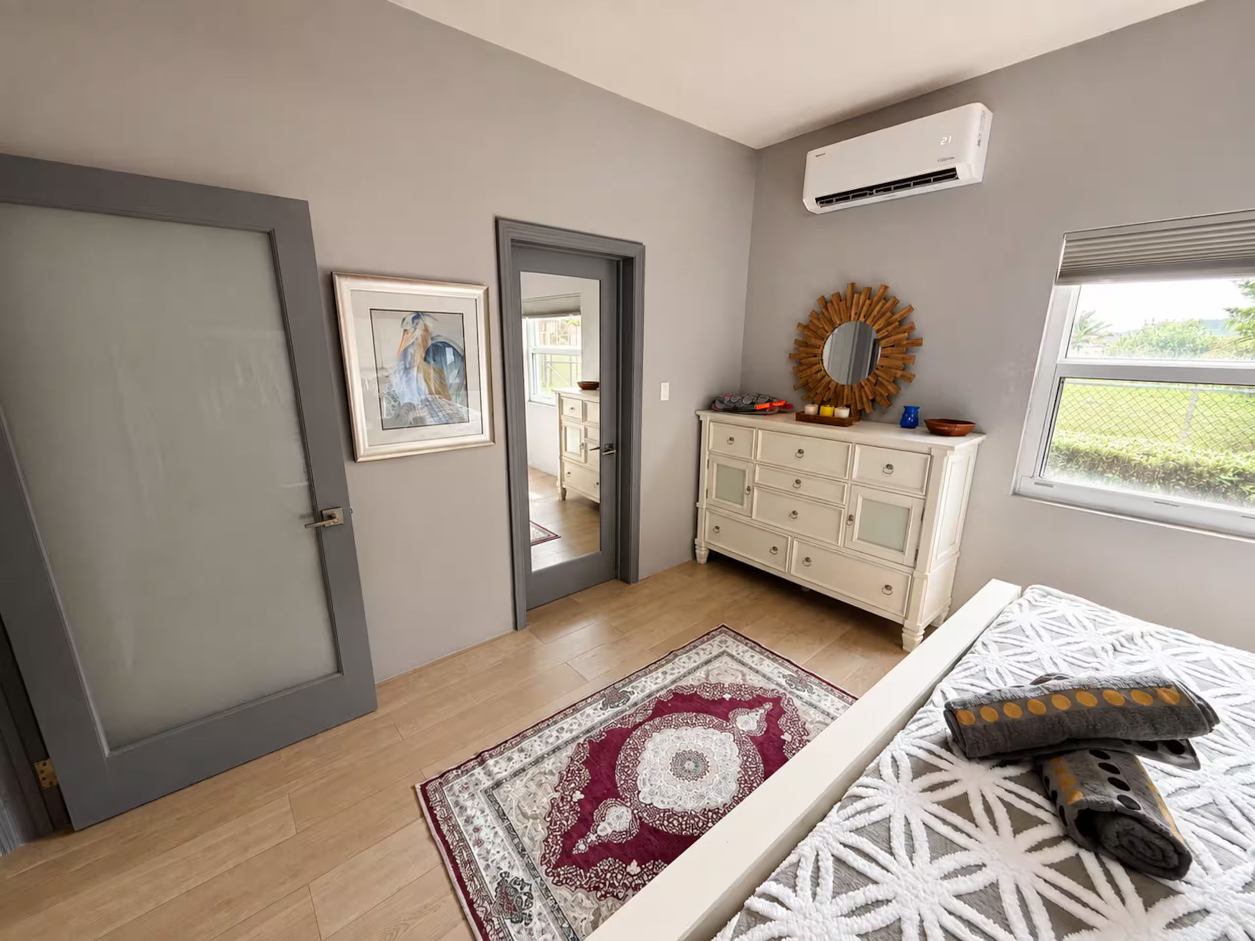 A room with a door, a dresser, a mirror, a rug, and a window.