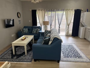 A living room with a blue sofa, a white coffee table, a patterned rug, a television, and a window with curtains. - Relaxing Luxury Villa Private Beach Pool AC WiFi (Turtle Bay)