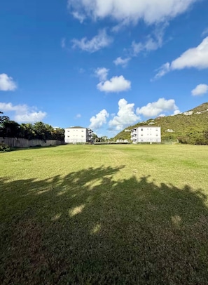 A grassy area with two white buildings, one with a balcony, and a clear sky. - Relaxing Luxury Villa Private Beach Pool-Gym-AC-WiFi-King Bed-Sleeper Sofa (Turtle Bay)
