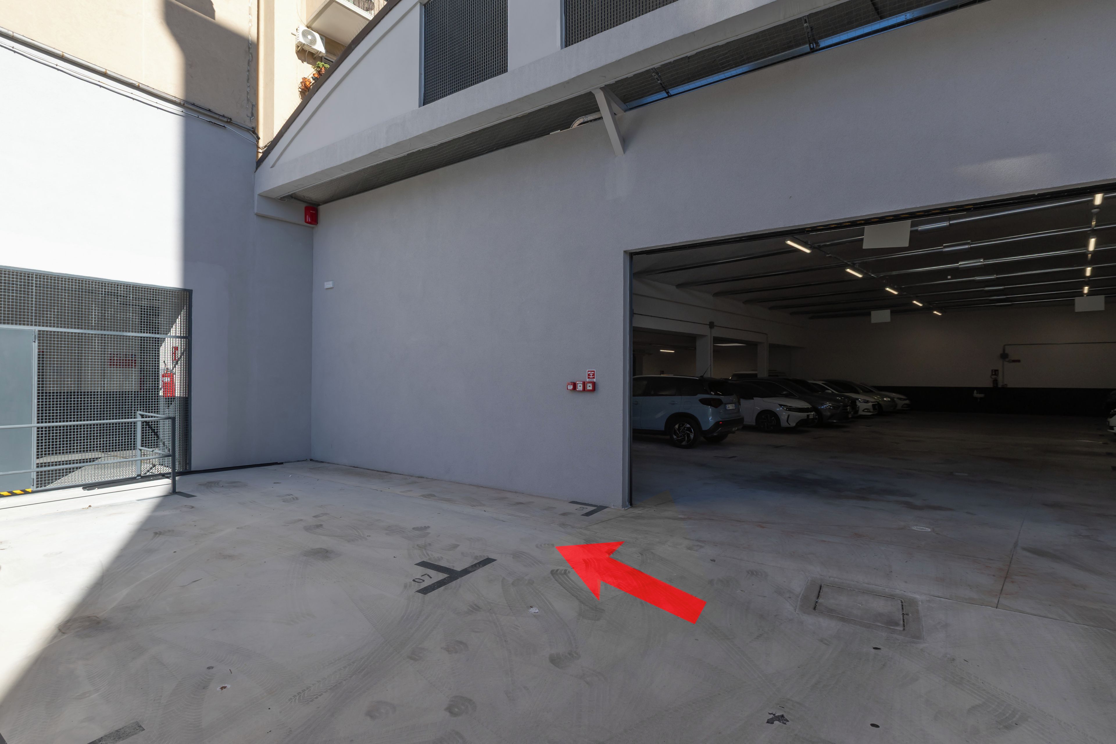 A parking garage entrance with a clear path marked by an arrow, a fire hydrant, and a metal gate.