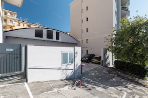 Un carrer estret amb una entrada tancada per una porta, un cotxe aparcat i un edifici amb façana plana.