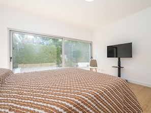 Een slaapkamer met een groot bed, een televisie en een schuifdeur naar een balkon.