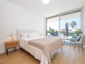 Een moderne slaapkamer met een groot bed, een nachtkastje met een lamp en uitzicht op het groen door een schuifdeur.
