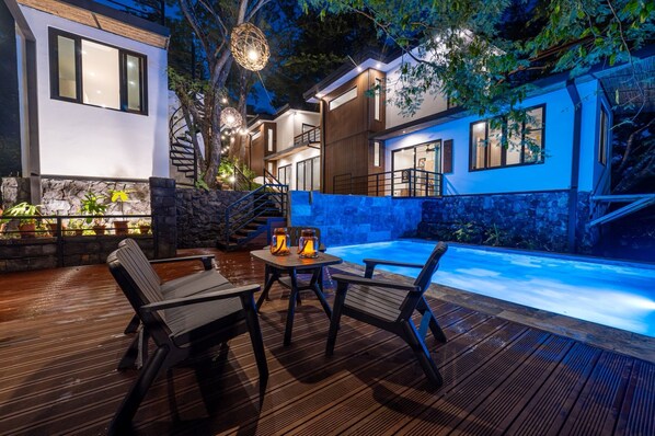 A modern outdoor pool area with wooden deck seating and a stone wall.