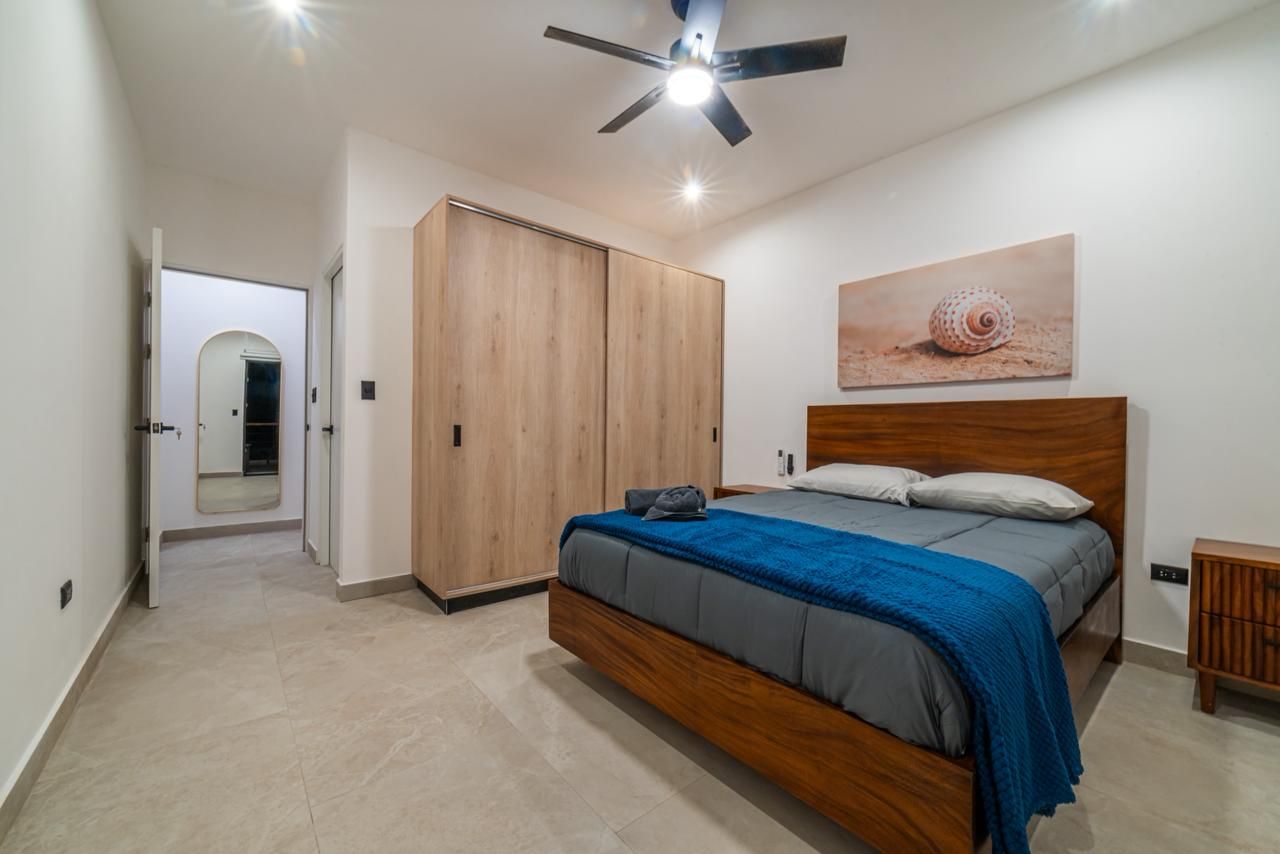 Une chambre à coucher avec un lit, une armoire, un ventilateur de plafond et un tableau accroché au mur.