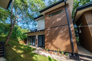Et moderne hus med to etager, en balkon, træfacade og en have med krukker.