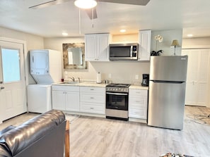 A modern kitchen with white cabinetry, a stainless steel refrigerator, a microwave, and a gas stove. - Guesthouse Bungalow near 31st St (Temple)