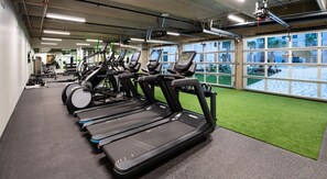 Ein Fitnessraum mit Laufbändern und Ergometer, großen Fenstern und Kunstrasenböden.