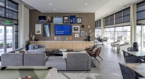 Eine moderne Lobby mit Billardtisch, bequemen Sitzgelegenheiten und einem großen Bildschirm, der eine Willkommensbotschaft zeigt.