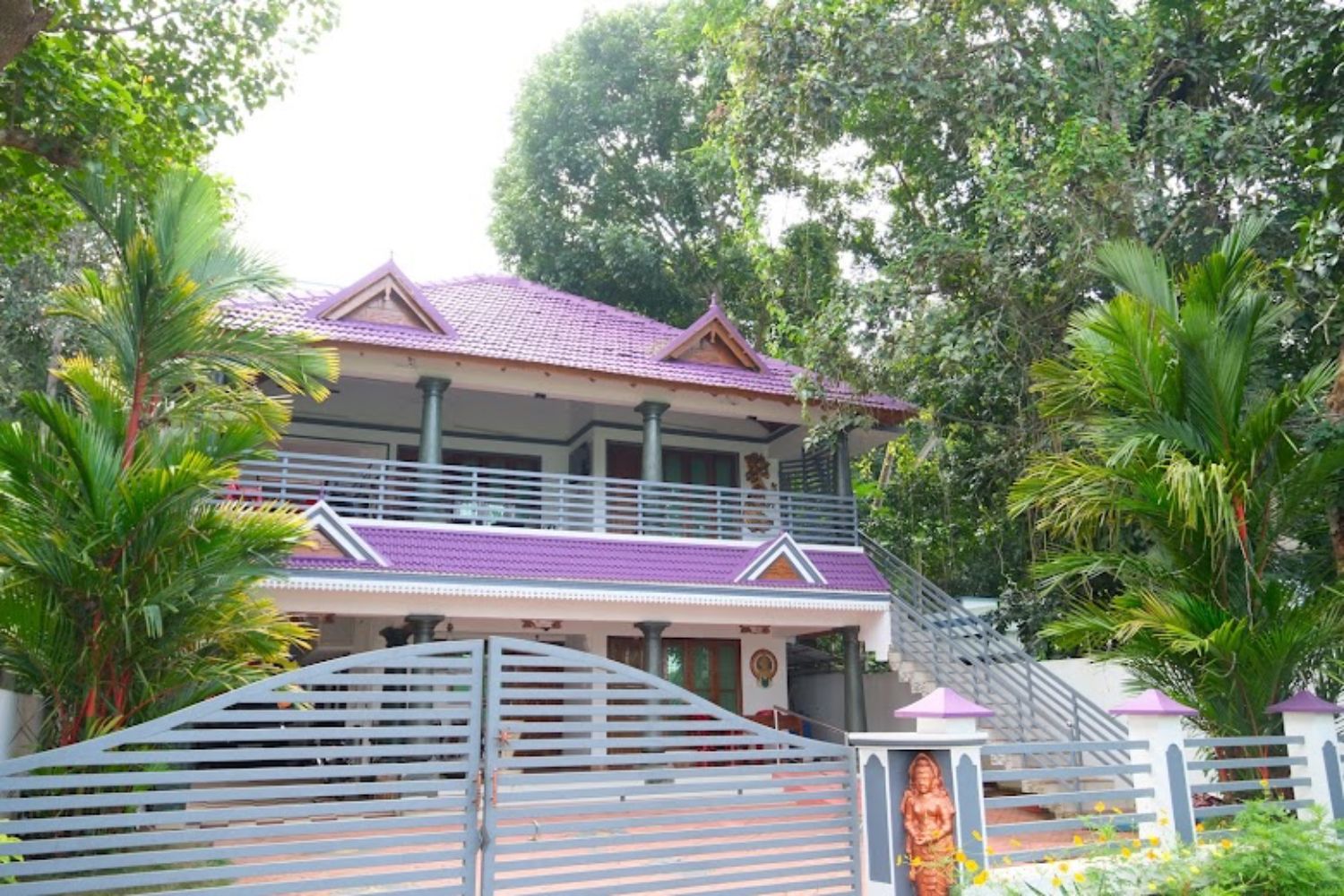 A two-story house with a balcony, surrounded by lush greenery.