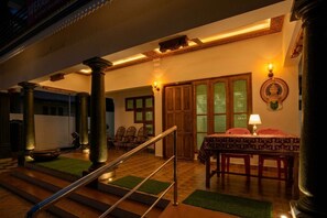 A staircase with a handrail leading to a room with a table and chairs, wooden columns, and a decorative wall.