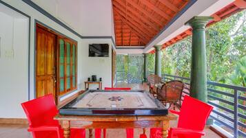 Une pièce avec une table en bois et des chaises rouges, un téléviseur accroché au mur et un balcon donnant sur un paysage verdoyant.