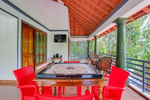 Una habitación con una mesa de madera y sillas rojas, un televisor en la pared y un balcón con vistas a zonas verdes.