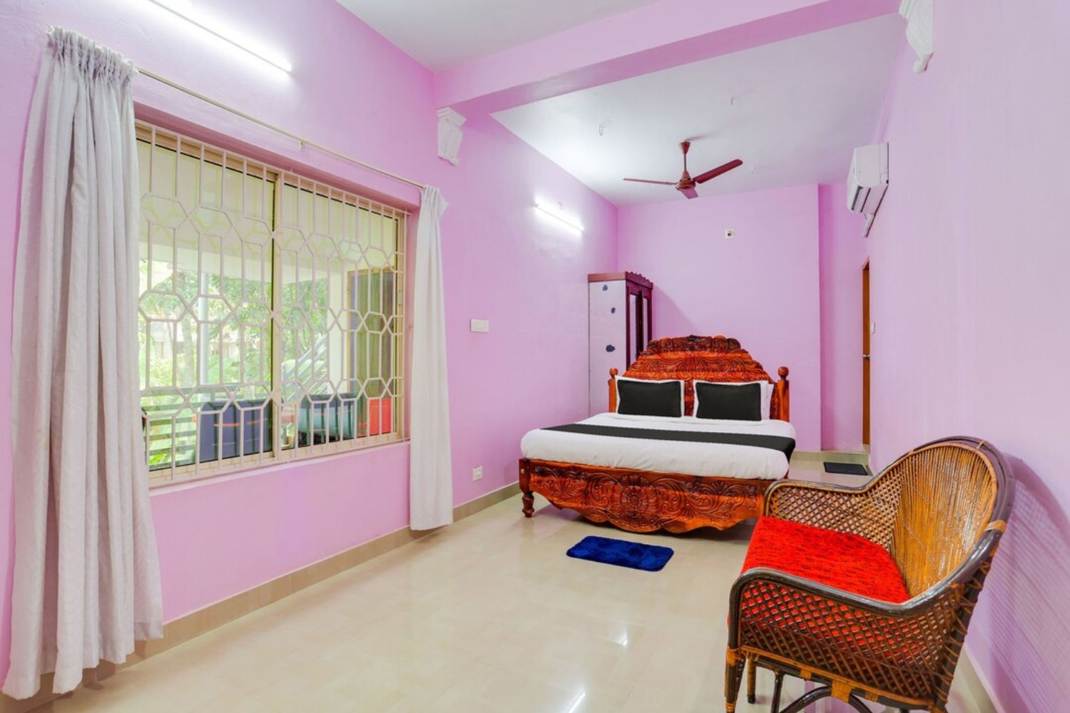 Un dormitorio con cama, una silla, armario y ventana con cortinas.