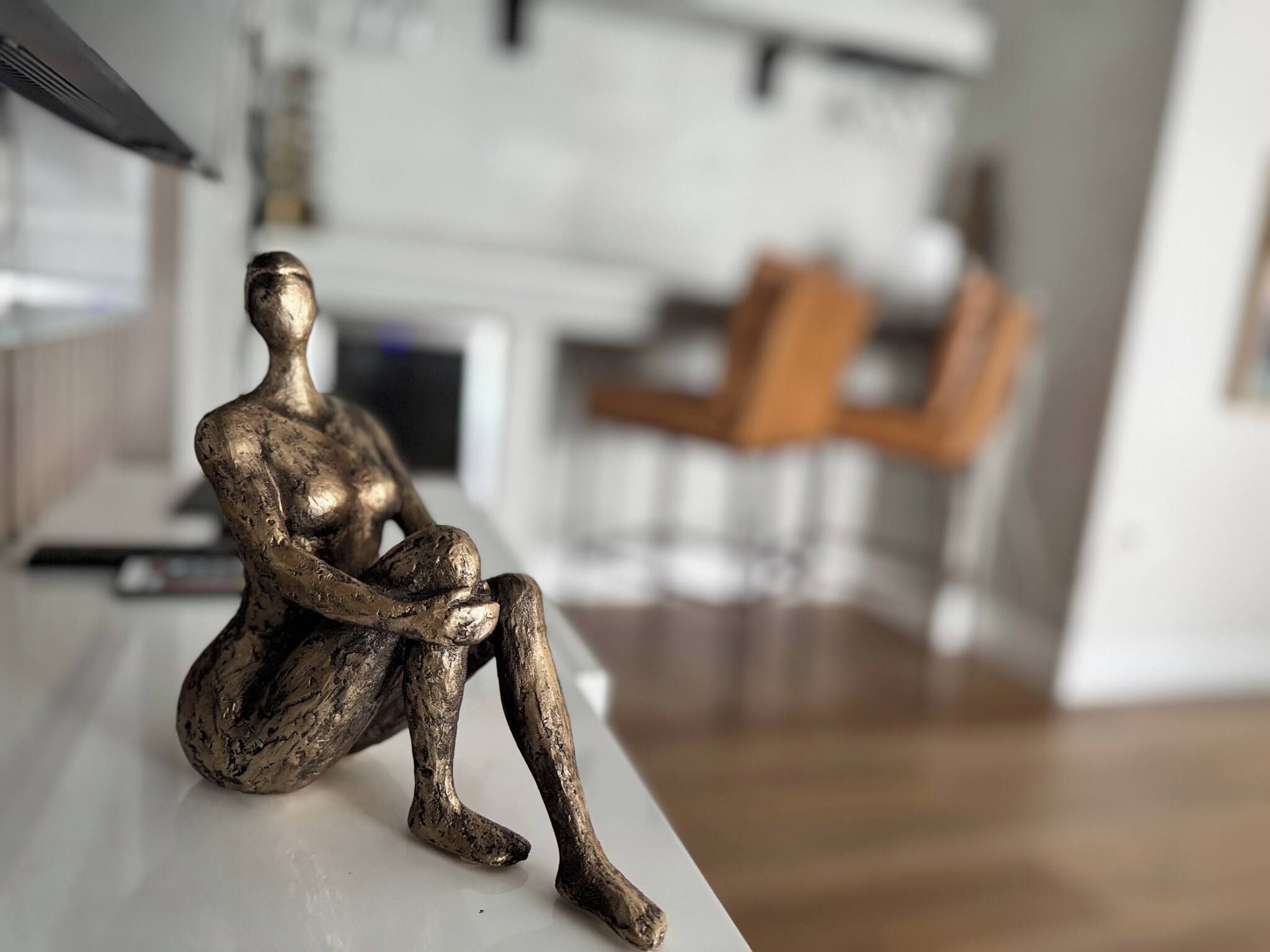 A bronze sculpture of a seated figure on a white surface in a modern interior space.