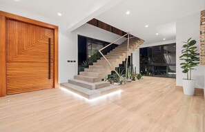 A modern interior with a wooden door, a staircase with a geometric railing, and a potted plant.