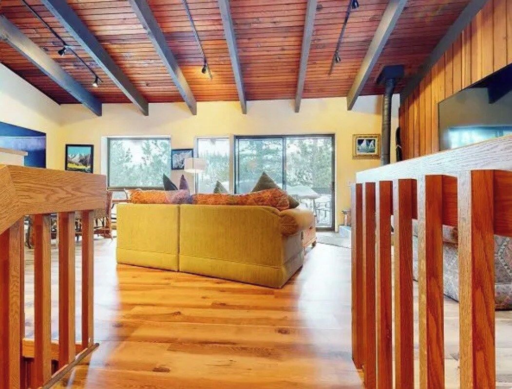 Ein großz ügiger Wohnbereich mit Holzboden, einem gelben Sofa und einer Holzwand.