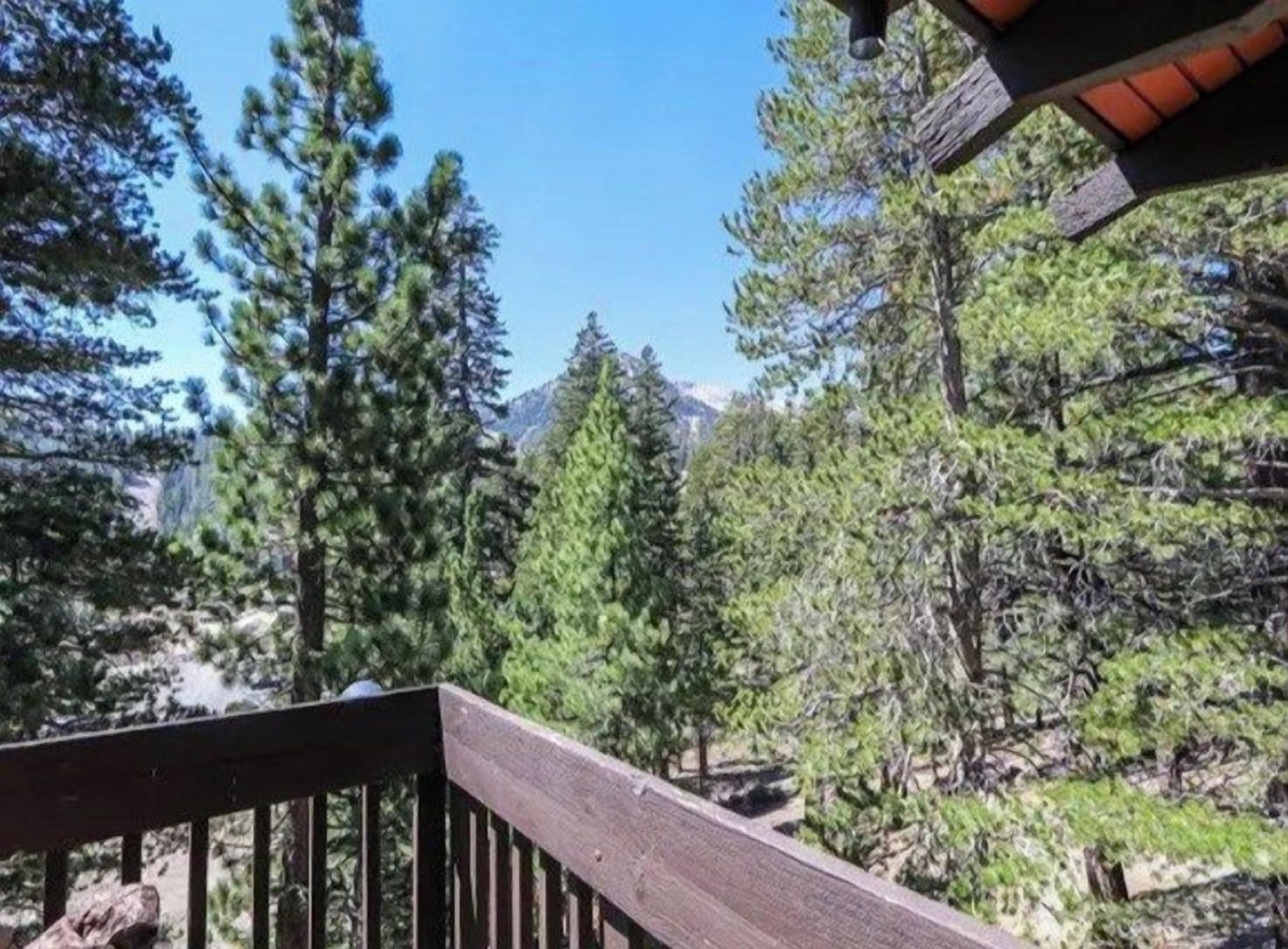A wooden deck with a view of dense forest and mountains in the distance.