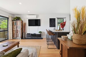 Een moderne keuken met een flatscreen-tv, een bar met krukken en een eethoek met een houten tafel en bank.