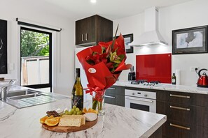 A modern kitchen with a marble countertop, a bouquet of flowers, a bottle of wine, and a variety of cheeses and fruits. - Whangaroa Landing - Lake Rotoma Holiday Home (Rotorua)