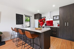 A modern kitchen with a central island, bar stools, dark cabinetry, and a red appliance. - Whangaroa Landing - Lake Rotoma Holiday Home (Rotorua)