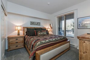 Une chambre à coucher avec un lit, des tables de chevet, une fenêtre avec des stores et un panneau accroché au mur.
