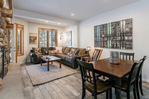 Een gezellige woonkamer met een open haard, een zithoek, een eettafel met stoelen en een groot abstract schilderij aan de muur.