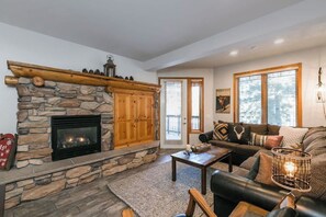A cozy living room with a stone fireplace, a wooden mantel, a leather sofa, and a coffee table. - Pet Friendly Mountain Hideaway (Mammoth Lakes)