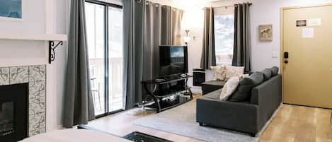 A modern living room with a sofa, TV, fireplace, and large windows.