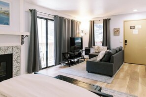 A modern living room with a sofa, TV, fireplace, and large windows. - Remodeled Mammoth Village Studio W/ Self Check In (Mammoth Lakes)