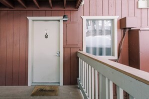 Eine weiße Tür mit der Nummer 19 und einer Fußmatte auf einer Holzveranda mit einem weißen Geländer.