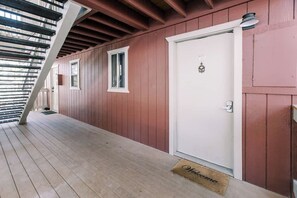 Um deck de madeira com uma porta branca e um tapete de boas-vindas.