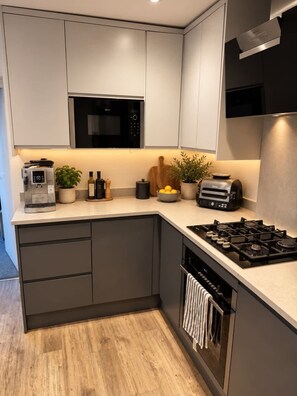 Een moderne keuken met een ingebouwde magnetron, een gasfornuis en een koffiezetapparaat.